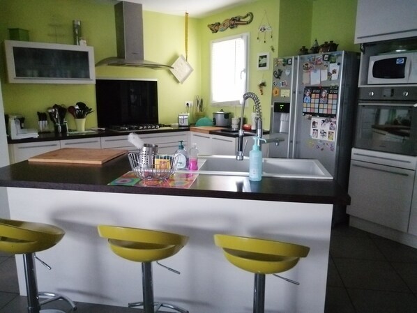 A kitchen with a central island, bar stools, a refrigerator, and a microwave.