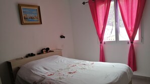 Un dormitorio con cama, mesita de noche, lámpara, un cuadro y cortinas rosas.
