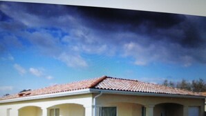 Una edificación de un solo nivel con techo de tejas, un porche cubierto con columnas y cielo despejado al fondo.