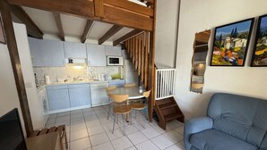 A modern kitchen with white cabinets, a dining area with a wooden table and chairs, a blue sofa, and a staircase leading to an upper level.
