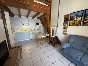 A modern kitchen with white cabinets, a dining area with a wooden table and chairs, a blue sofa, and a staircase leading to an upper level.