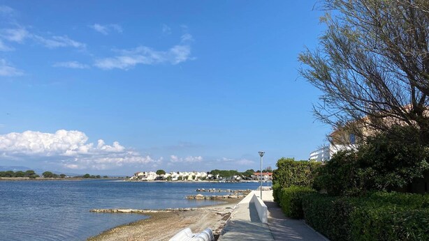 A coastal walkway with a clear view of the sea, a row of buildings in the background, and a lamppost along the path.