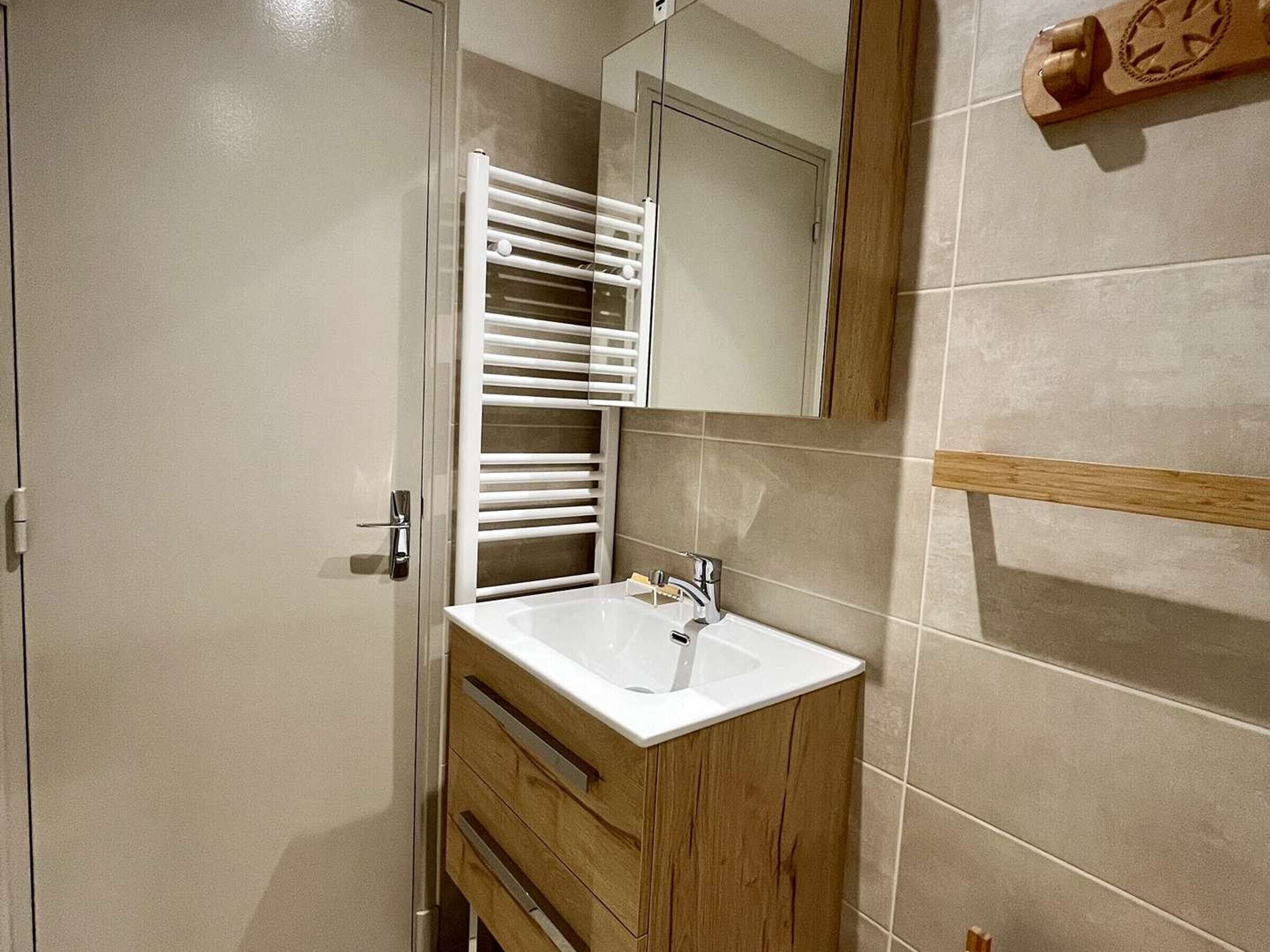 Une salle de bain avec un lavabo blanc, des meubles en bois, un porte-serviettes et un miroir.