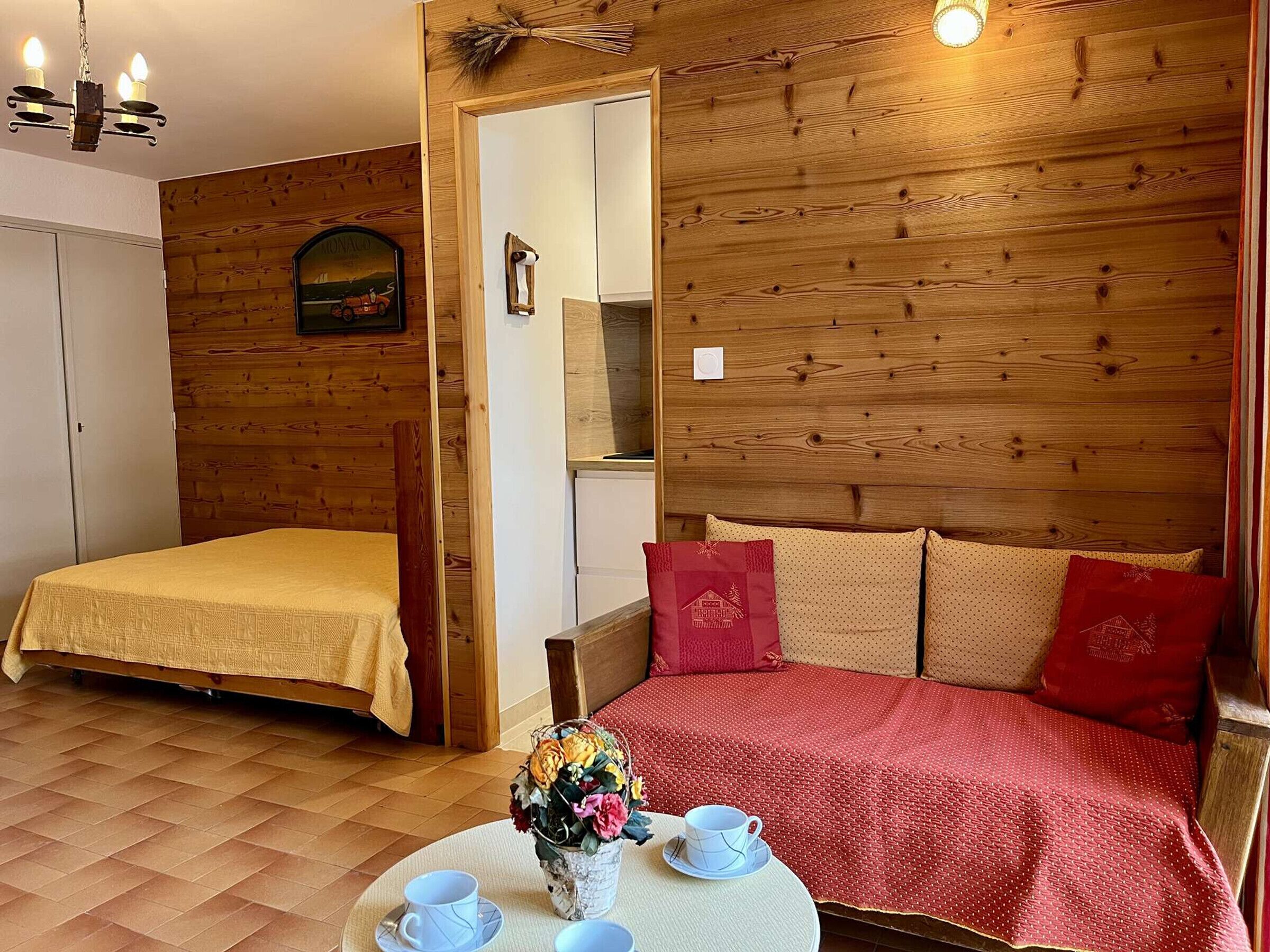 A cozy room with a bed, a small table with cups and a vase of flowers, and wooden walls.