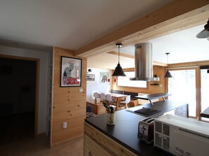 Et moderne køkken med trævægge, et spiseområde med bord og stole, og et stort vindue der giver naturligt lys.