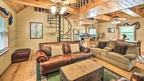 A spacious living room with two sofas, a coffee table, and a ceiling fan. A staircase leads to an upper level, and a kitchen is visible in the background. - Golfer's Retreat at Kudzu Cove Cabins Resort (Guntersville)