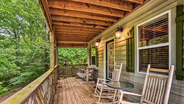 A wooden porch with a table and chairs, surrounded by a wooden railing, overlooking a forested area. - Golfer's Retreat at Kudzu Cove Cabins Resort (Guntersville)