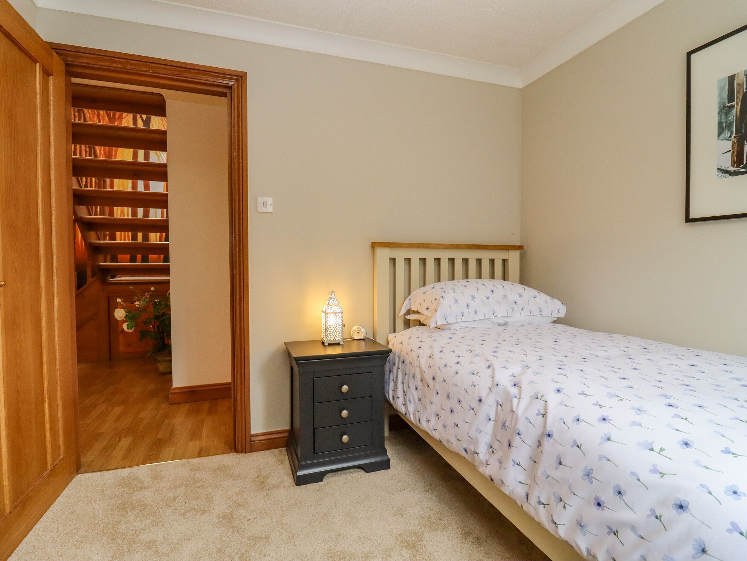 A bedroom with a bed, a nightstand, a wall-mounted clock, and a bookshelf.