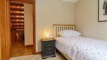 A bedroom with a bed, a nightstand, a wall-mounted clock, and a bookshelf.