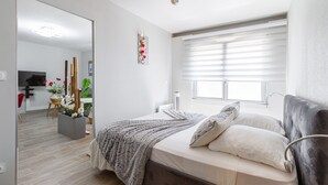 A bedroom with a bed, a window with blinds, a bedside table, and a mirror. - Quiet 1-bed with office space, Saint-Cyprien, 200m to metro (Toulouse)
