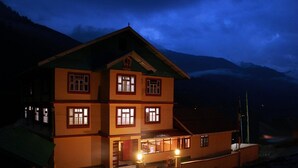 A multi-story building with multiple windows and a balcony, set against a mountainous backdrop. - Rufina Norling Zimkhang (Chungthang)