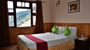 A hotel room with a wooden bed, a view of mountains through the window, and a nightstand with a book. - Rufina Norling Zimkhang (Chungthang)