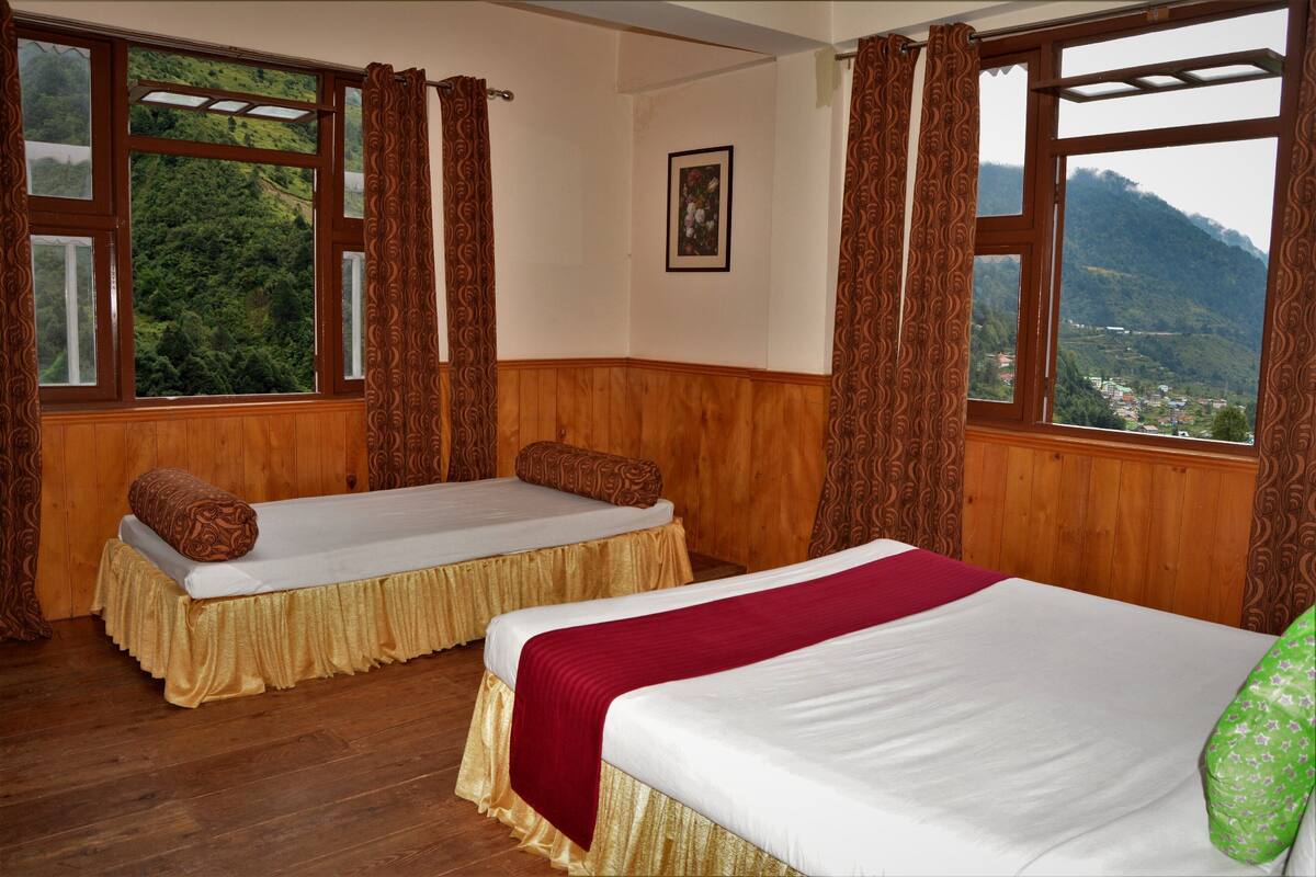 A room with two beds, wooden walls, large windows with curtains, and a view of a mountainous landscape.