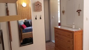 Huoneessa on puinen lipasto, peili, tyynyillä varustettu sänky, puinen seinäkoriste ja ovi, joka johtaa toiseen huoneeseen.