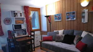 Tunnelmallinen olohuone, jossa on puusein ä, sohva, sohvapöytä, televisio ja ikkuna, jossa on verhot.