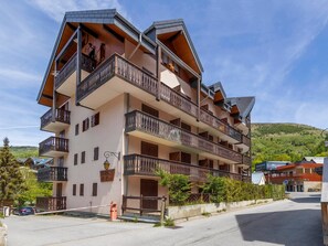 Un hotel de varios pisos con balcones, un estacionamiento y montañas al fondo.