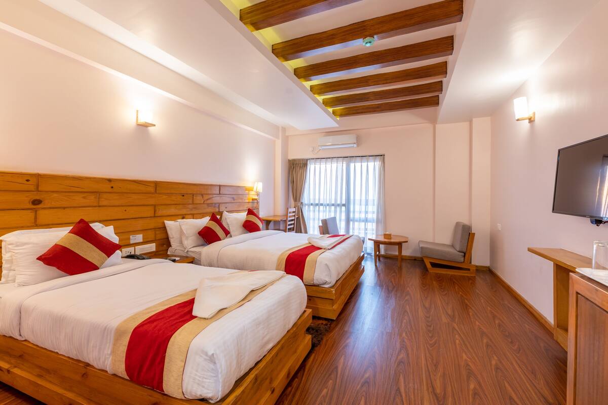 A hotel room with two wooden beds, a TV, a small table, and a chair.