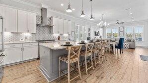 A spacious kitchen with white cabinets, a large island, and wooden chairs. - Song By the Sea - Steps to the Beach, Gated, Sleeps 14! (Miramar Beach)