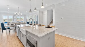 A spacious kitchen with a large island, modern pendant lights, and a view of the outdoors through large windows. - Song By the Sea - Steps to the Beach, Gated, Sleeps 14! (Miramar Beach)