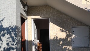 A residential building with a tiled exterior, a set of concrete steps leading to a door, and a small outdoor area with a metal railing.
