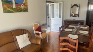 A living room with a brown leather sofa, a dining table set for four, and a painting on the wall.