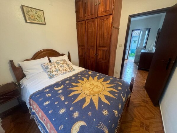 A bedroom with a bed, wooden wardrobe, and a door leading to another room.