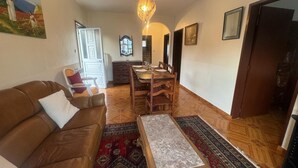 A cozy living room with a brown leather sofa, a wooden coffee table, and a dining area with a wooden table and chairs.