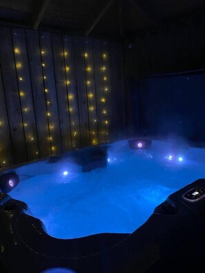 A hot tub with blue lighting, surrounded by wooden panels with string lights.