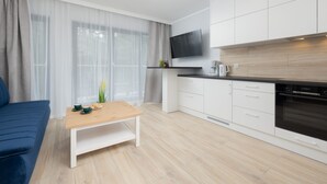 Une cuisine moderne avec des armoires blanches, un four encastré et un téléviseur à écran plat fixé au-dessus du plan de travail.