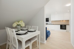 Une cuisine moderne avec des meubles blancs, un coin repas avec des chaises blanches et un canapé bleu.