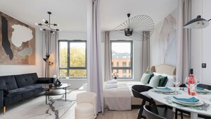 Ein modernes Wohnzimmer mit einem schwarzen Sofa, einem runden Couchtisch, einem weißen Sessel und einem Essbereich mit gedecktem Tisch für zwei Personen.