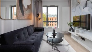 Ein modernes Wohnzimmer mit einem dunklen Sofa, einem runden Couchtisch und einem großen Fernseher an einer weißen Wand.