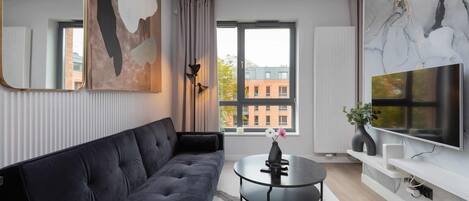 A modern living room with a dark sofa, a round coffee table, and a large TV on a white wall.