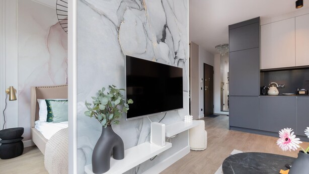 Ein modernes Wohnzimmer mit einem großen Flachbildfernseher an einer Marmorwand, einem weißen Konsolentisch mit einer Vase und einem schwarzen Pouf.