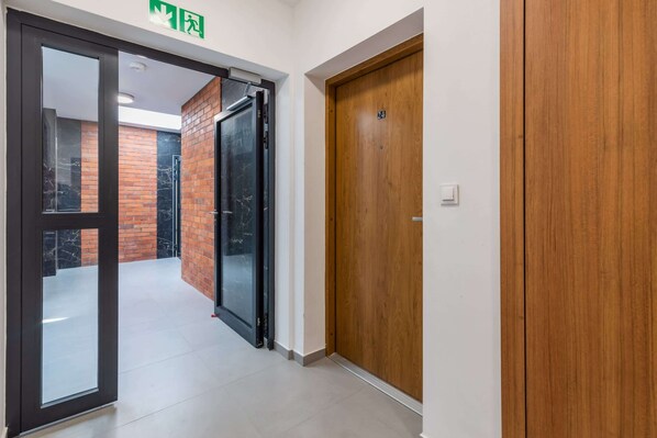 A hallway with a glass door leading to a balcony, a wooden door, and a brick wall.