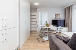 Una sala de estar moderna con un sofá, una mesa de comedor con sillas, un televisor y una puerta que da a otra habitación.