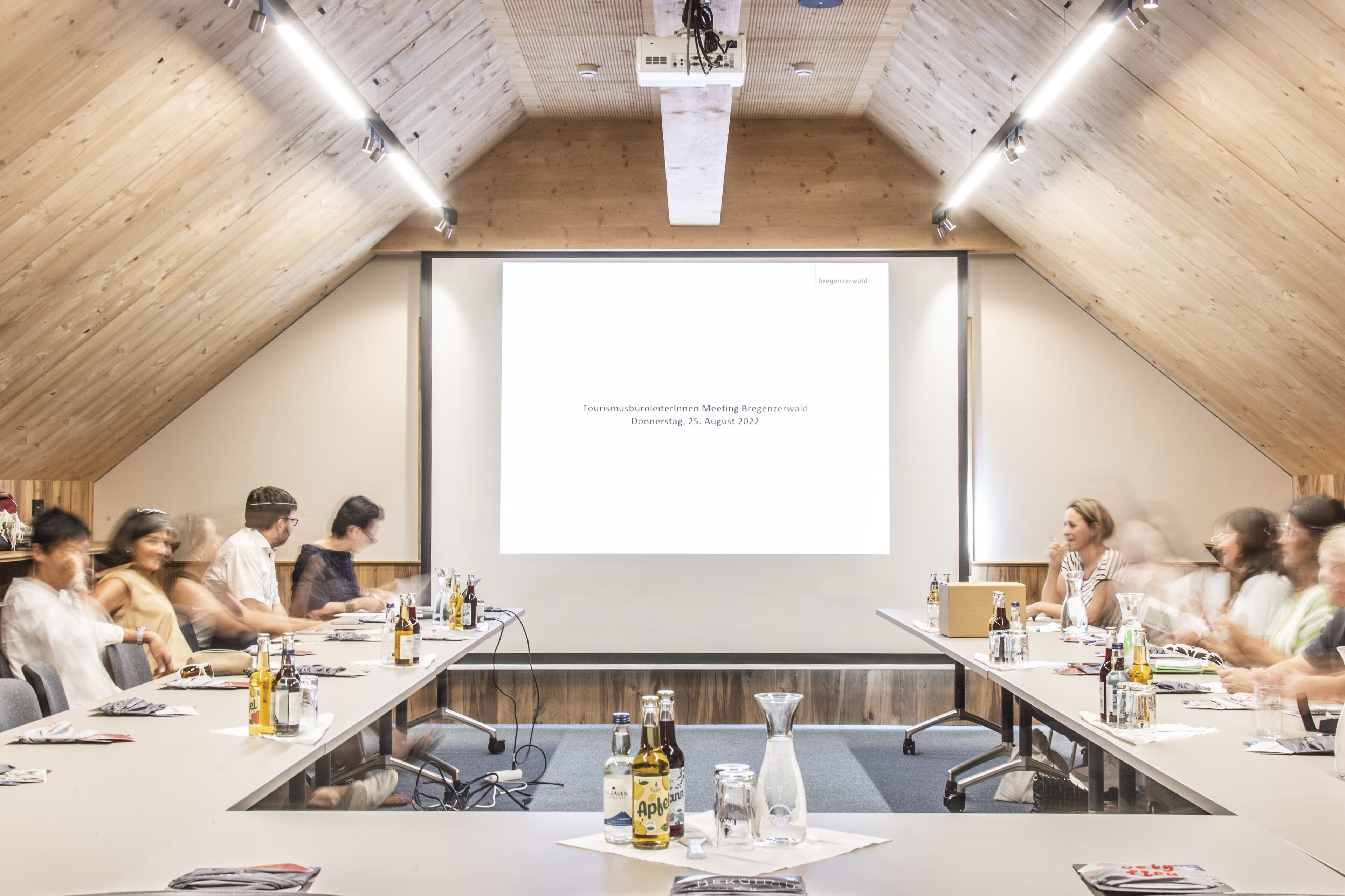 A conference room with a long table, chairs, and a projector screen displaying text.