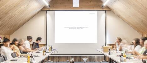A conference room with a long table, chairs, and a projector screen displaying text.