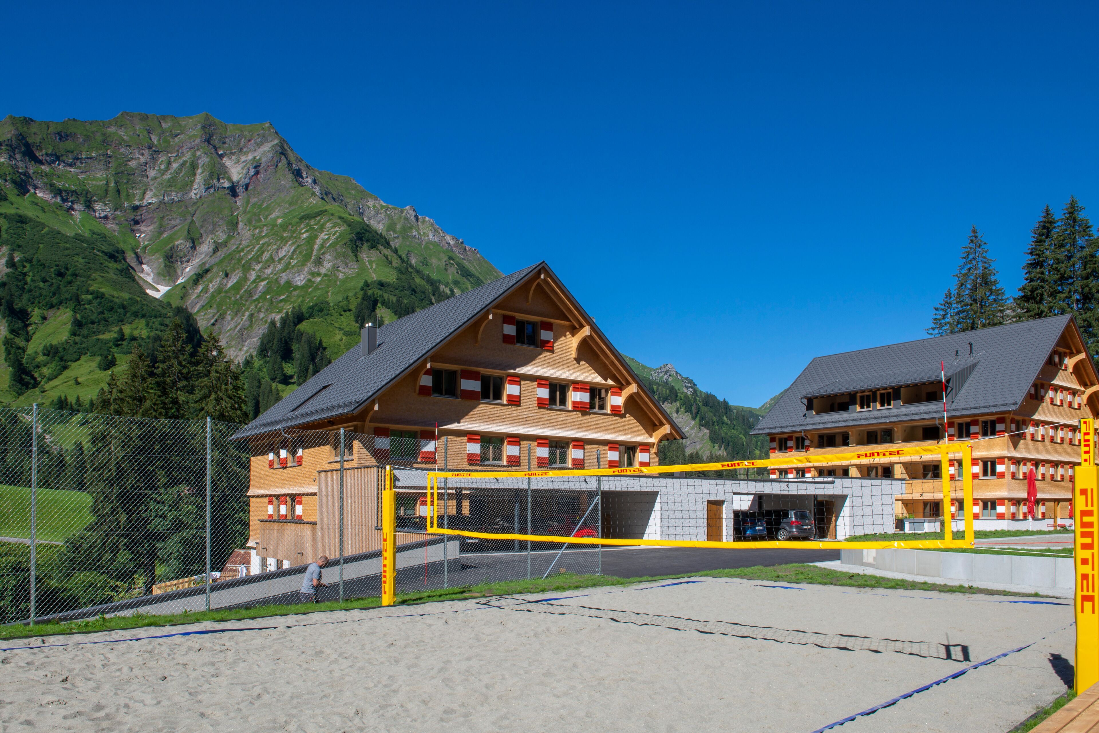 A mountain lodge with a wooden exterior, a tennis court, and a view of the surrounding mountains.
