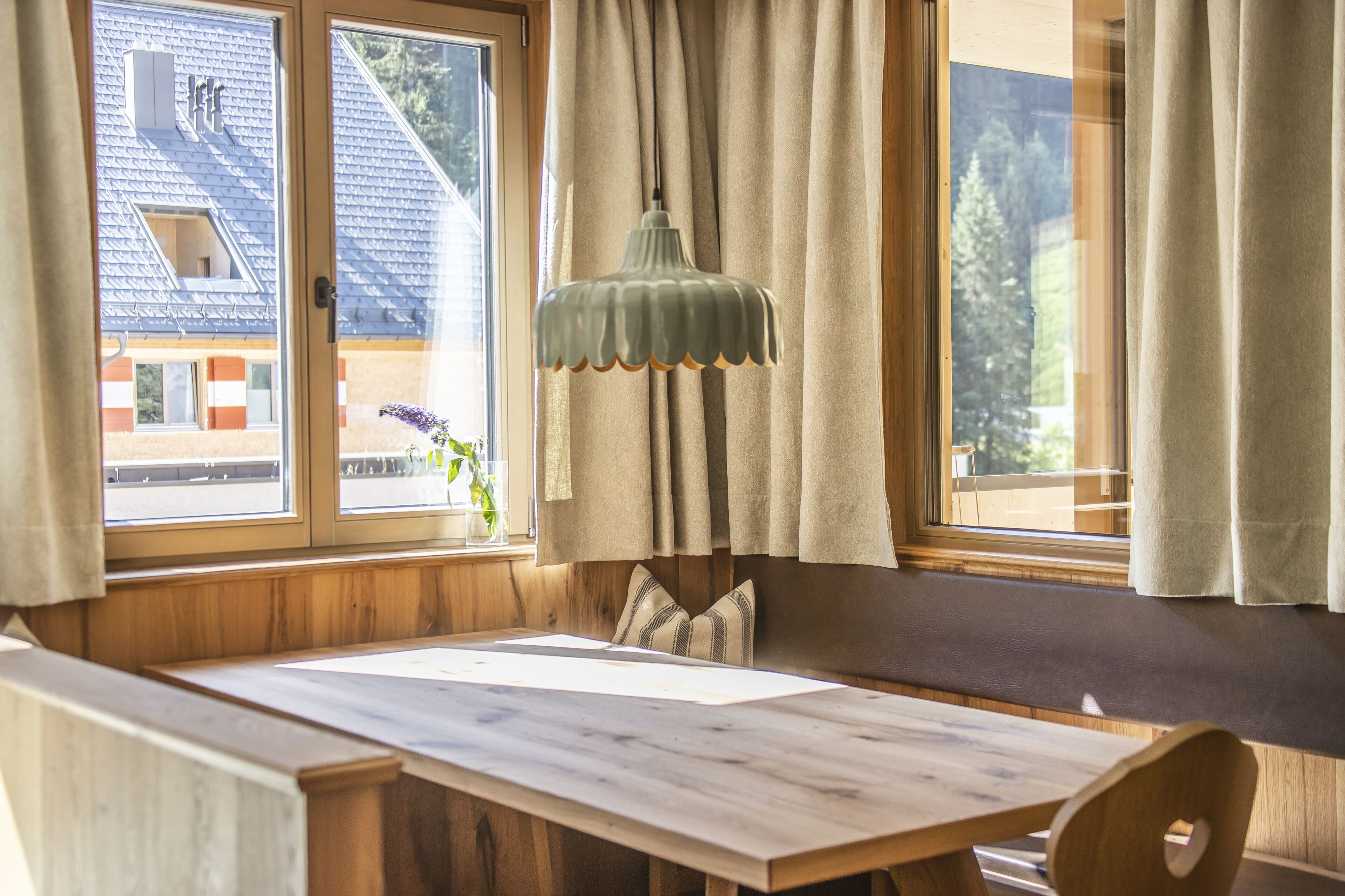 A wooden bench with a table in front of a window with curtains.