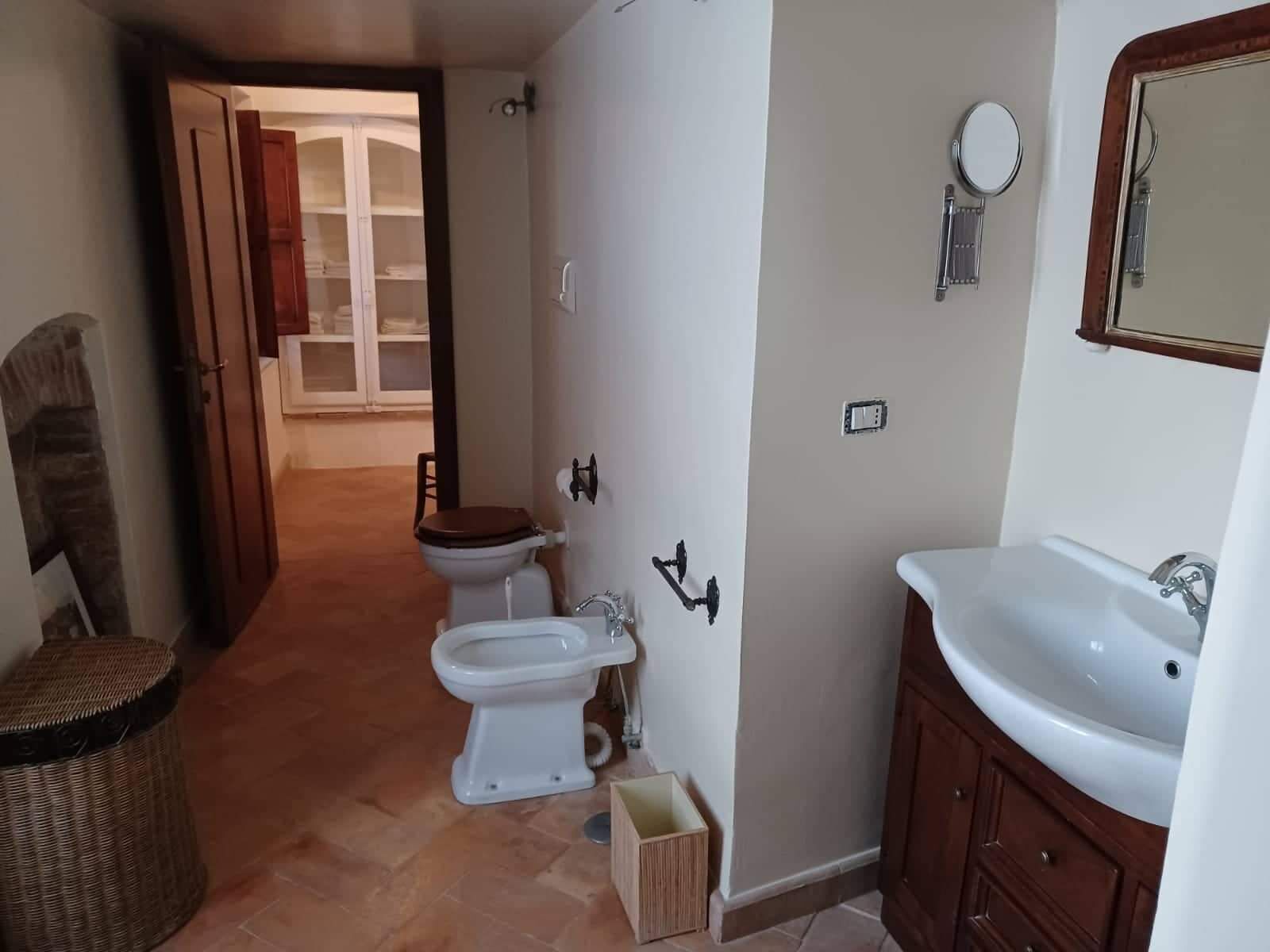 Een badkamer met toilet, bidet, wastafel en spiegel. Er staat een rieten mand en een klein houten doos op de vloer.
