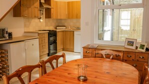 Une cuisine avec des meubles de rangement en bois, une cuisinière et un coin repas comprenant une table et des chaises en bois.