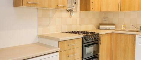 Una cocina con armarios de madera, estufa a gas, horno y lavavajillas.