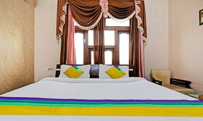 A hotel room with a bed, a chair, and a window with curtains. - Itsy Hotels Friends (Haldwani)