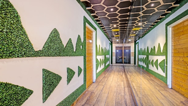 A hallway with a wooden floor, green wall designs, and a hexagonal ceiling pattern. - Itsy Hotels Friends (Haldwani)
