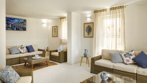 A spacious living room with two sofas, a coffee table, and a rug. There are framed pictures on the walls and a window with curtains. - Mercury Beach Hotel (Sant'Antioco)