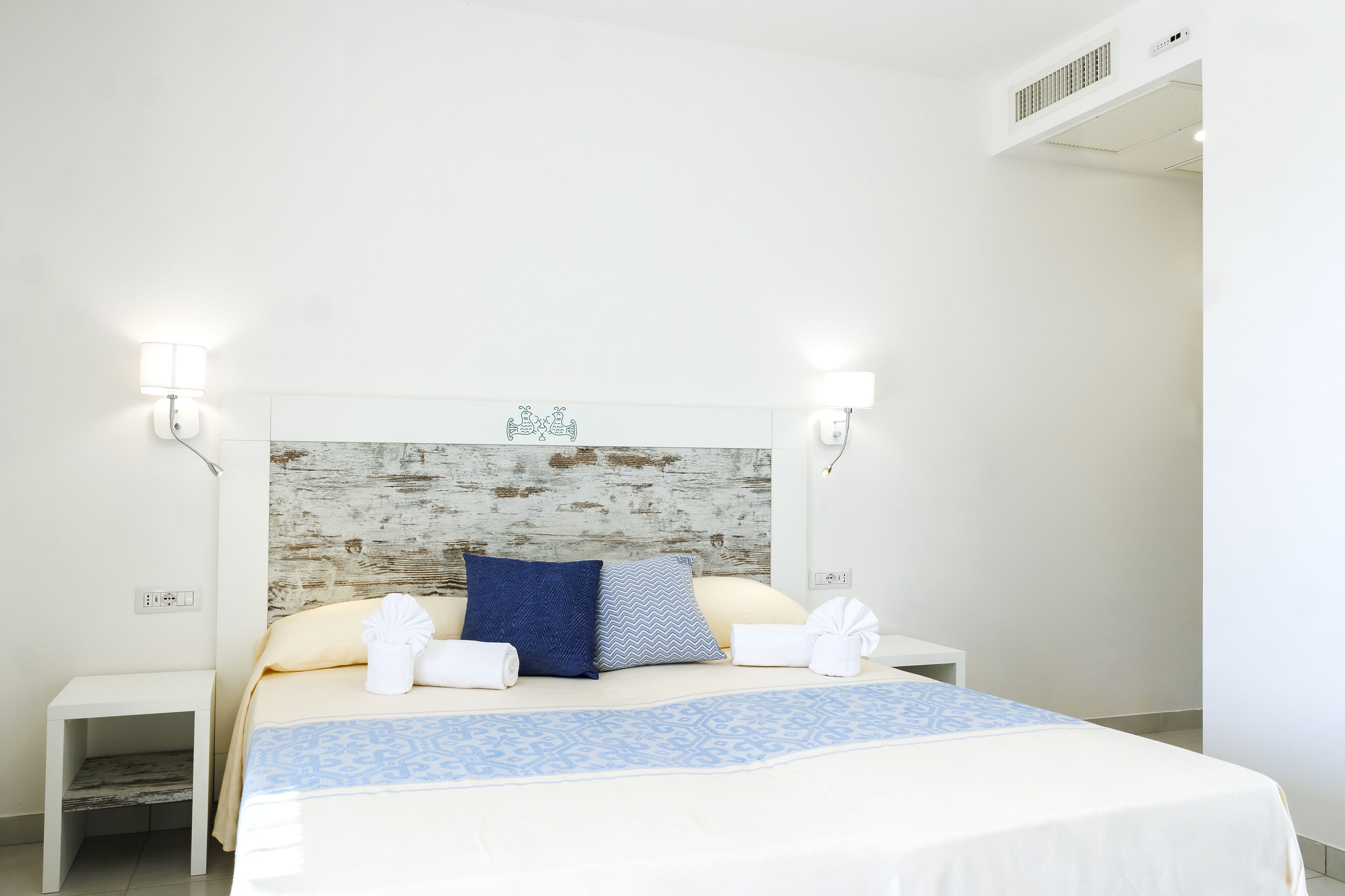 A neatly arranged hotel room with a bed, two bedside tables, and wall-mounted lights.
