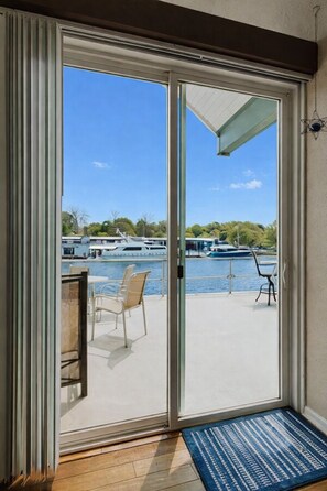 Porta de correr de vidro que dá para um deck externo, com vista para barcos em um corpo de água.