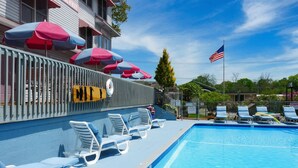 Una piscina con sillas de descanso y sombrillas, un flotador salvavidas y una bandera estadounidense.