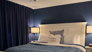Un dormitorio con cama blanca, paredes azul oscuro, ventilador de techo y dos lámparas de noche.